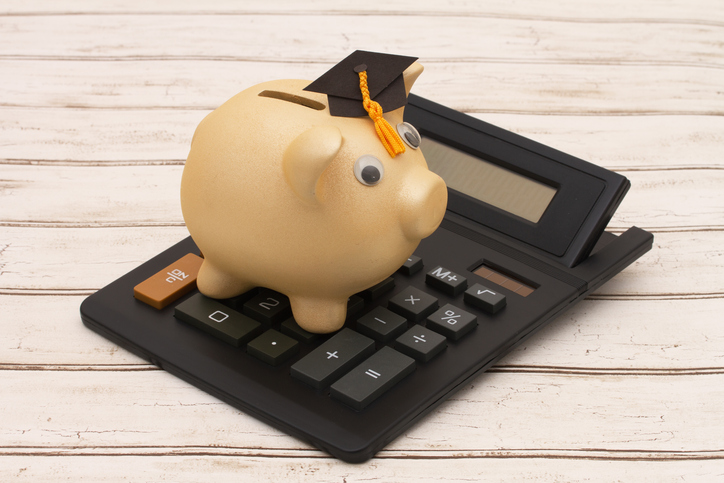 Cost of education, A golden piggy bank with grad cap and calculator on a wood background
